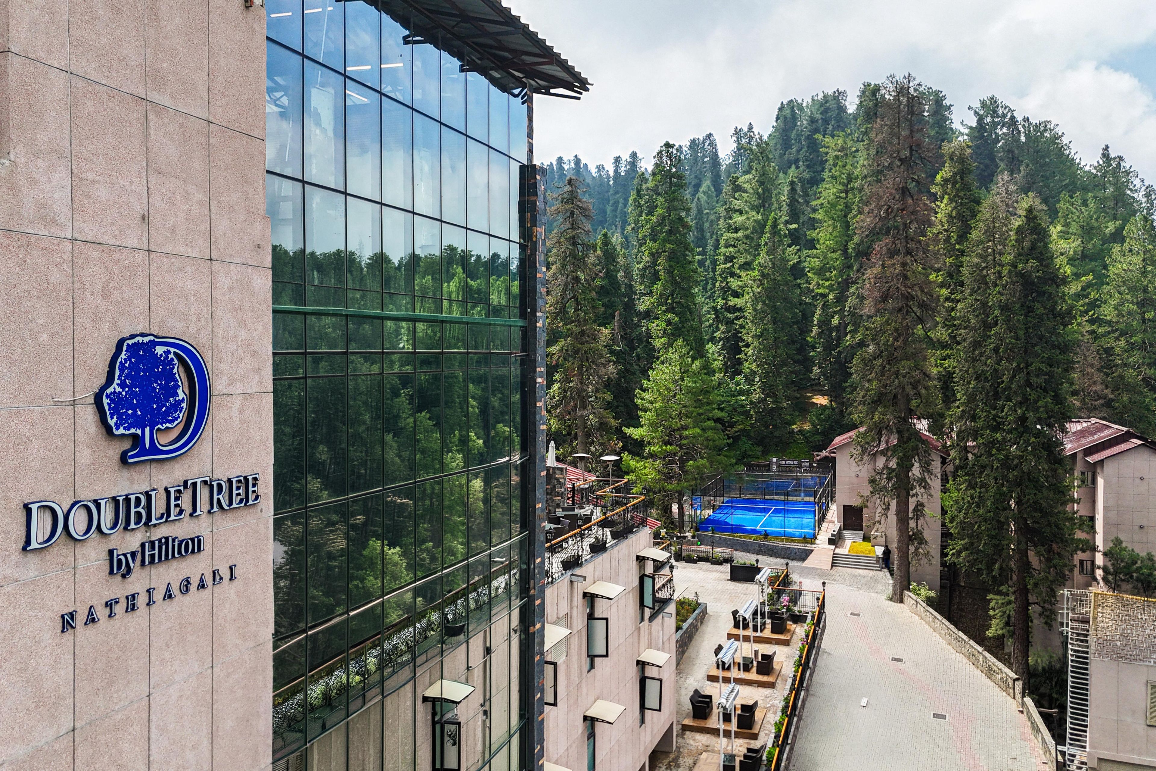A hotel with a glass facade, outdoor seating area, and a tennis court.
