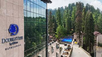A hotel with a glass facade, outdoor seating area, and a tennis court.