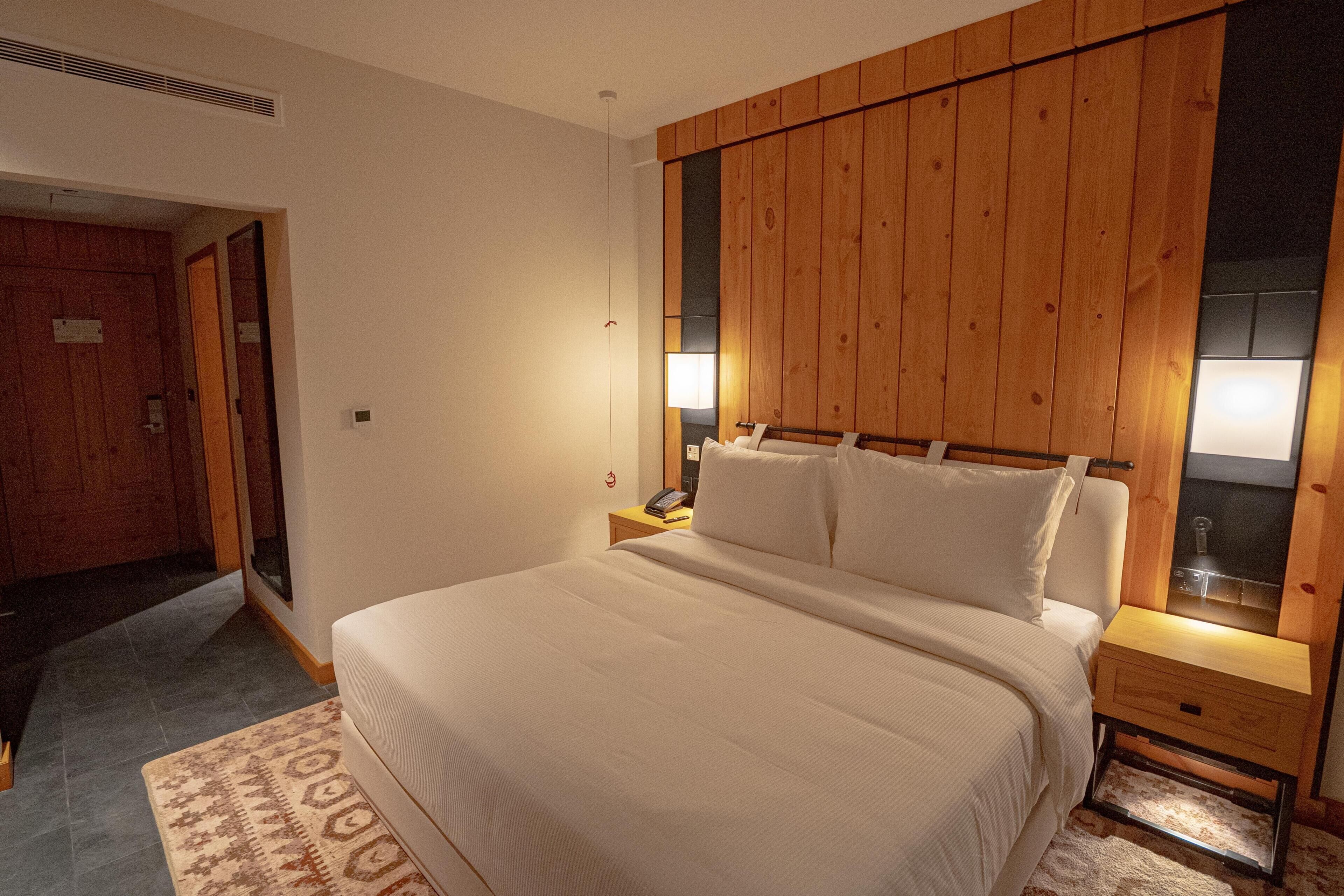 A bedroom with a large bed, wooden headboard, bedside lamps, and a small bedside table.