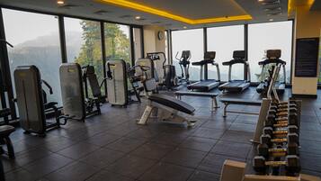 Un gimnasio con diferentes equipos de ejercicio, amplias ventanas y vistas a montañas.