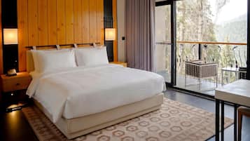 A bedroom with a large bed, wooden panel walls, a nightstand, a bedside lamp, and a view of a balcony with outdoor furniture.