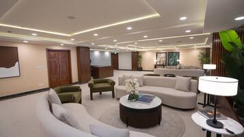 A modern hotel lobby with a curved sofa, a round coffee table, and a TV mounted on the wall.