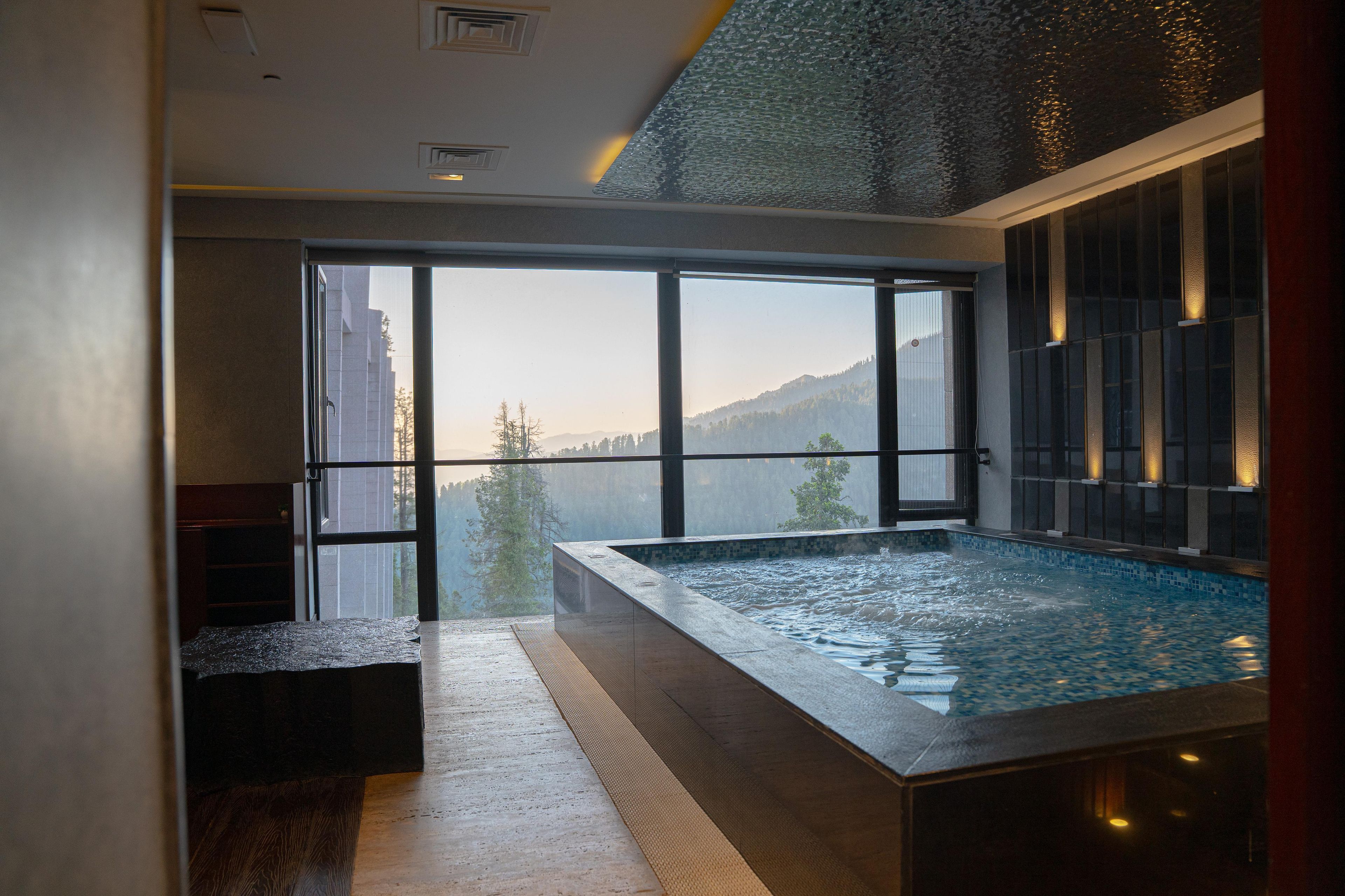 A modern indoor swimming pool with a glass wall providing a view of a mountainous landscape.