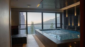 A modern indoor swimming pool with a glass wall providing a view of a mountainous landscape.