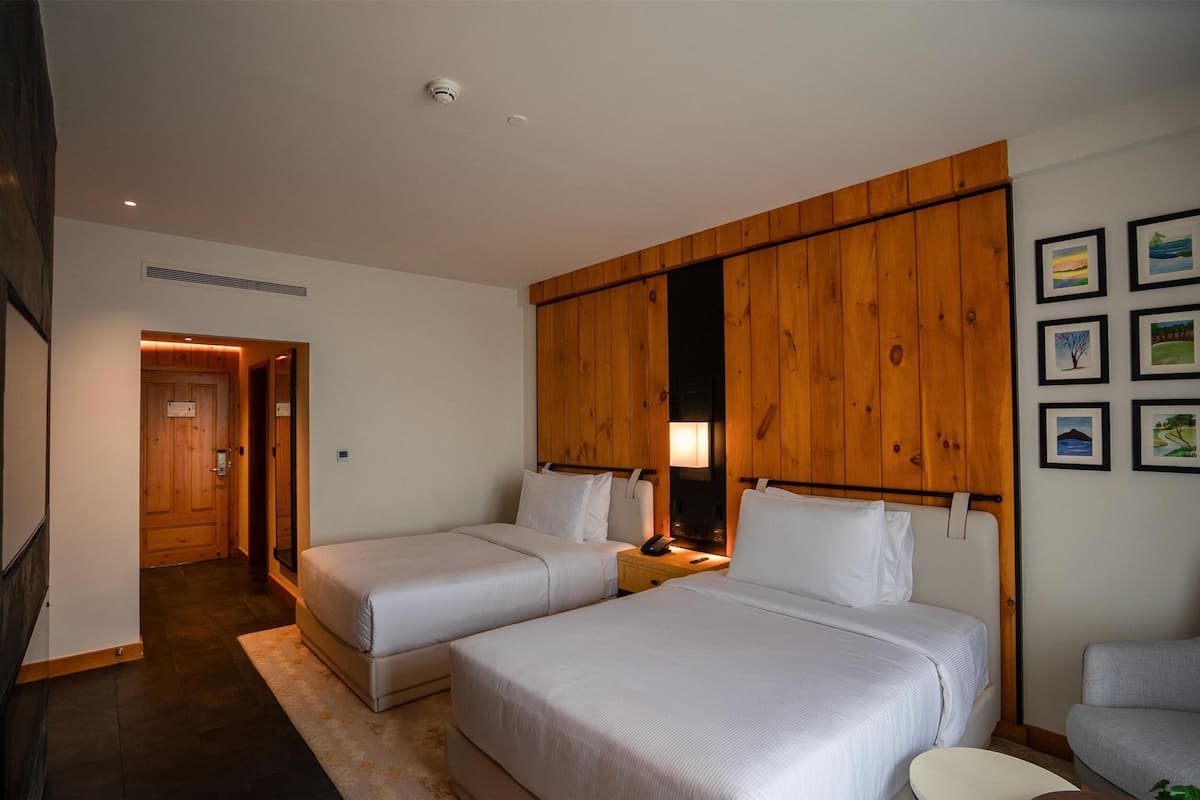 Een hotelkamer met twee bedden, houten paneelbekleding aan de muur, een nachtkastje met een lamp en ingelijste foto's.