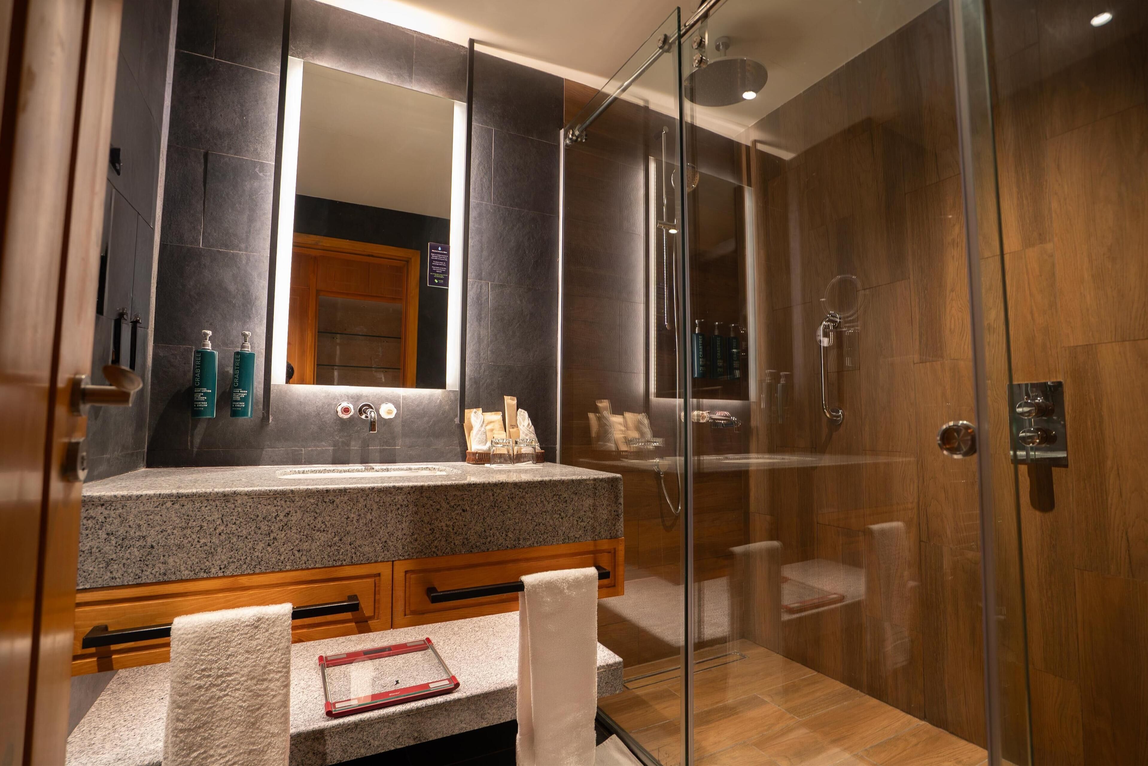 Une salle de bain moderne avec un comptoir en granit, un grand miroir, une douche à parois de verre et des meubles en bois.