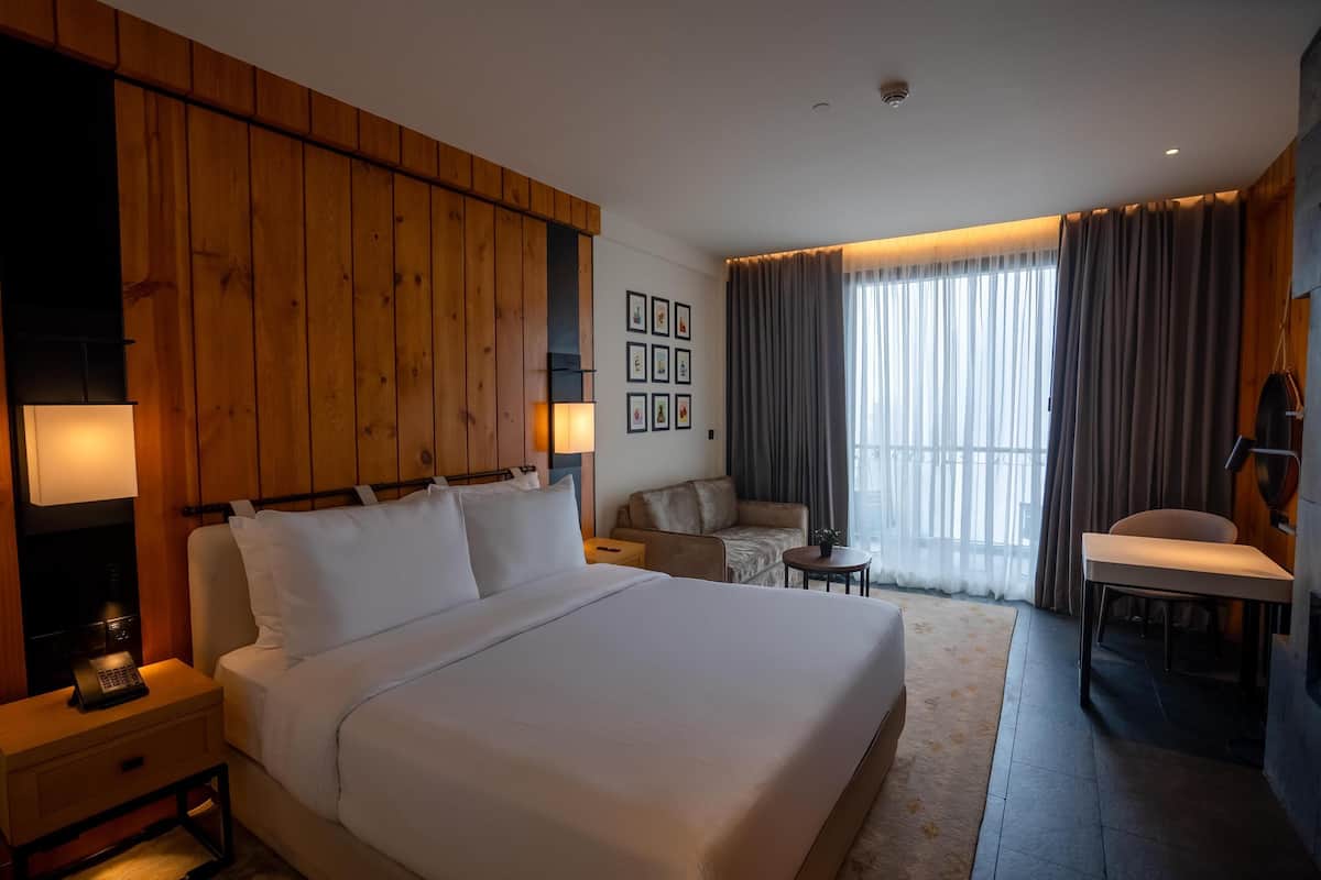 Een hotelkamer met een groot bed, een houten hoofdbord, een bureau, een stoel, een bijzettafeltje en een bank.