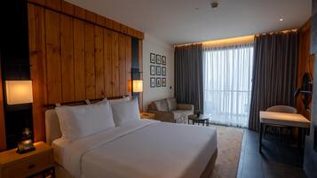 Una habitación de hotel con una cama grande, un cabecero de madera, un escritorio, una silla, una mesita y un sofá.