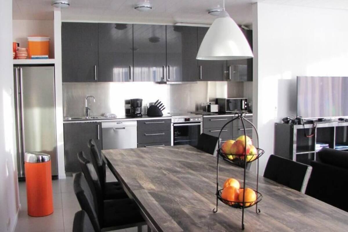 A modern kitchen with dark cabinets, a wooden dining table, and a fruit bowl.