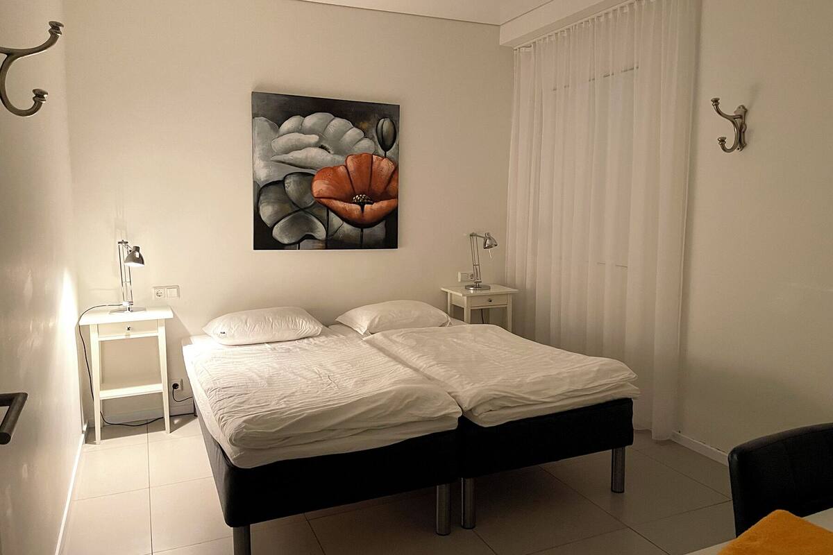 A modern bedroom with a bed, two bedside tables, a nightstand, a painting, and a window with curtains.