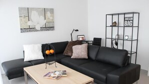 A modern living room with a black leather sofa, a wooden coffee table, and a black metal shelving unit with the text "DREAM BIG". - Halllandsnes Apartments (Akureyri)