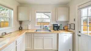 Una cocina con gabinetes blancos, encimera de madera, lavavajillas integrado y ventana con vista a una cerca de madera.
