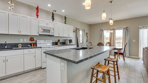 A modern kitchen with white cabinets, a large island, bar stools, and pendant lighting. - 7 Mi to Golf: Mtn-View Retreat in Bullhead City (Bullhead City)