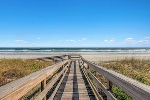 Une promenade en bois menant à une plage, avec un ciel dégagé.