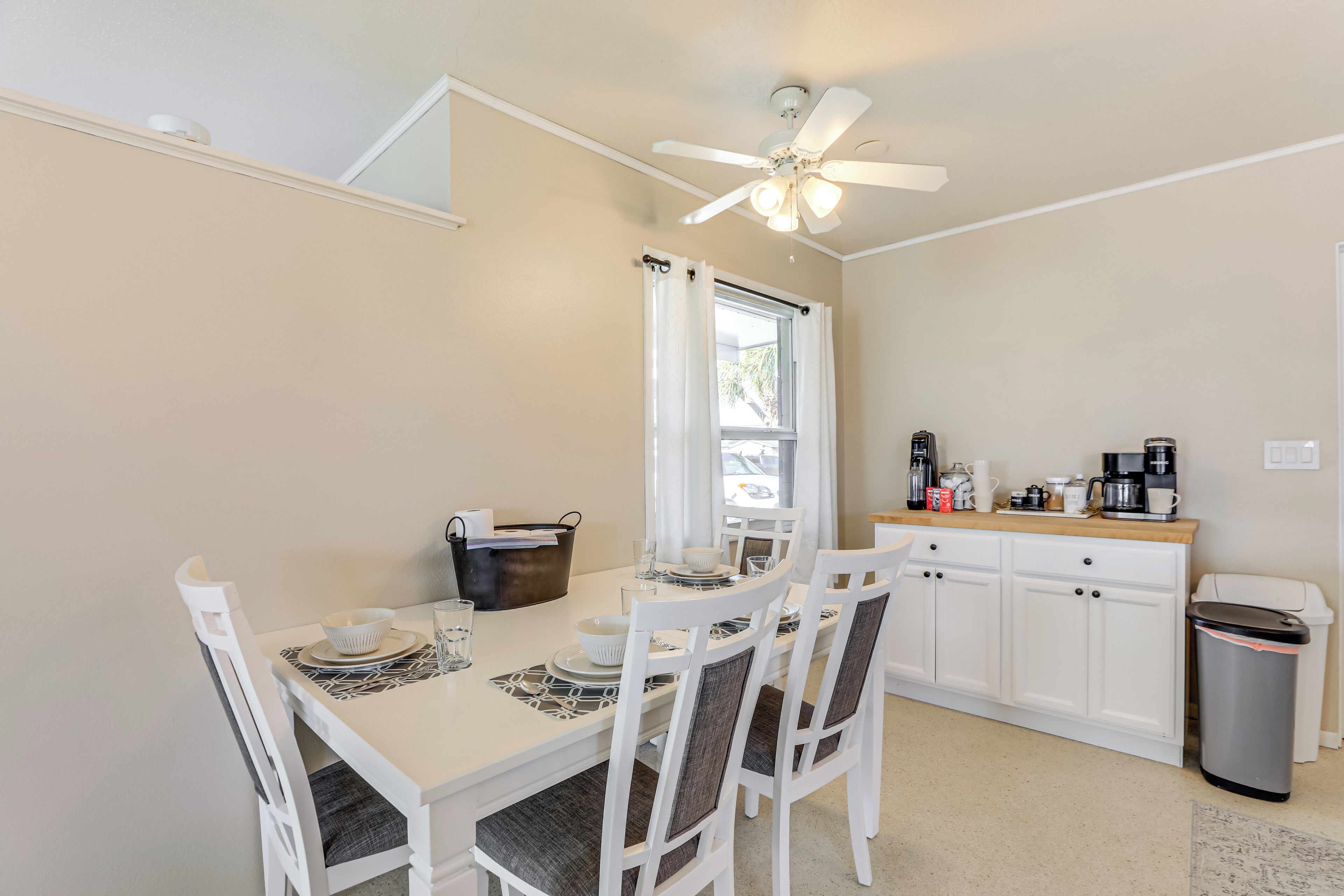 A compact kitchen with a dining table, chairs, a ceiling fan, and a window with curtains.