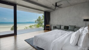 A modern bedroom with a large bed, a ceiling fan, and a view of the beach. - Vows Villa Beachfront (Koh Samui)