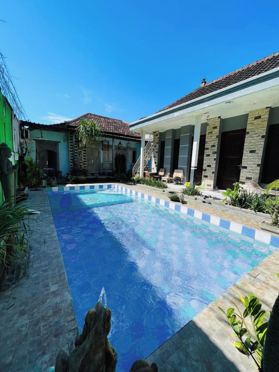 A swimming pool with a tiled deck, surrounded by a building with a tiled roof and stone accents.