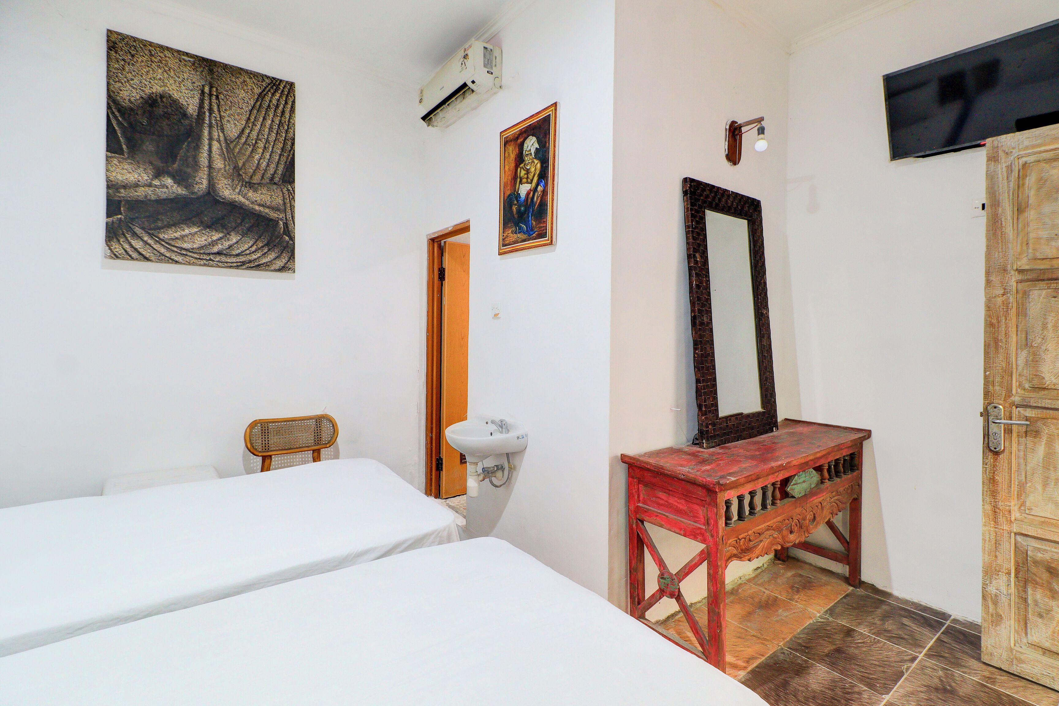 Een kamer met twee bedden, een houten console, een spiegel, een wastafel en een schilderij aan de muur.
