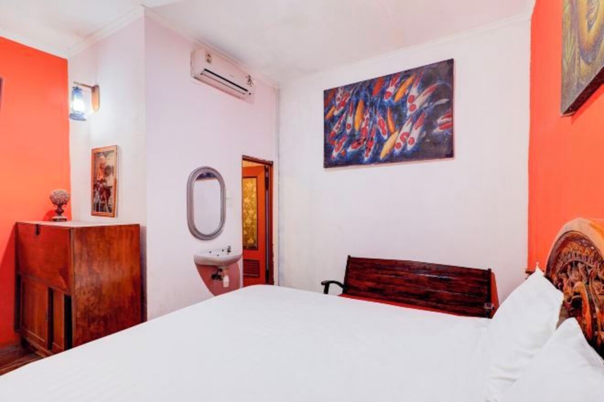 A hotel room with a bed, a wooden dresser, a sink, a mirror, and a painting on the wall.
