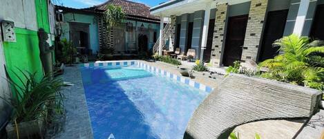A swimming pool with a tiled deck, surrounded by a house with a tiled roof and a covered porch.