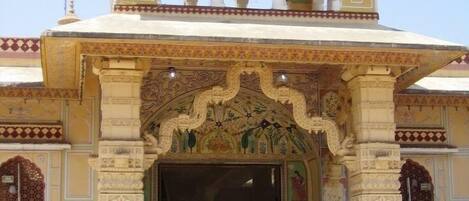 A building with ornate architecture, featuring a large entrance with detailed carvings and a balcony with a patterned roof.