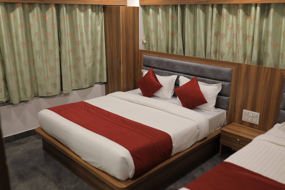 A hotel room with a large bed, two bedside tables, and green patterned curtains.