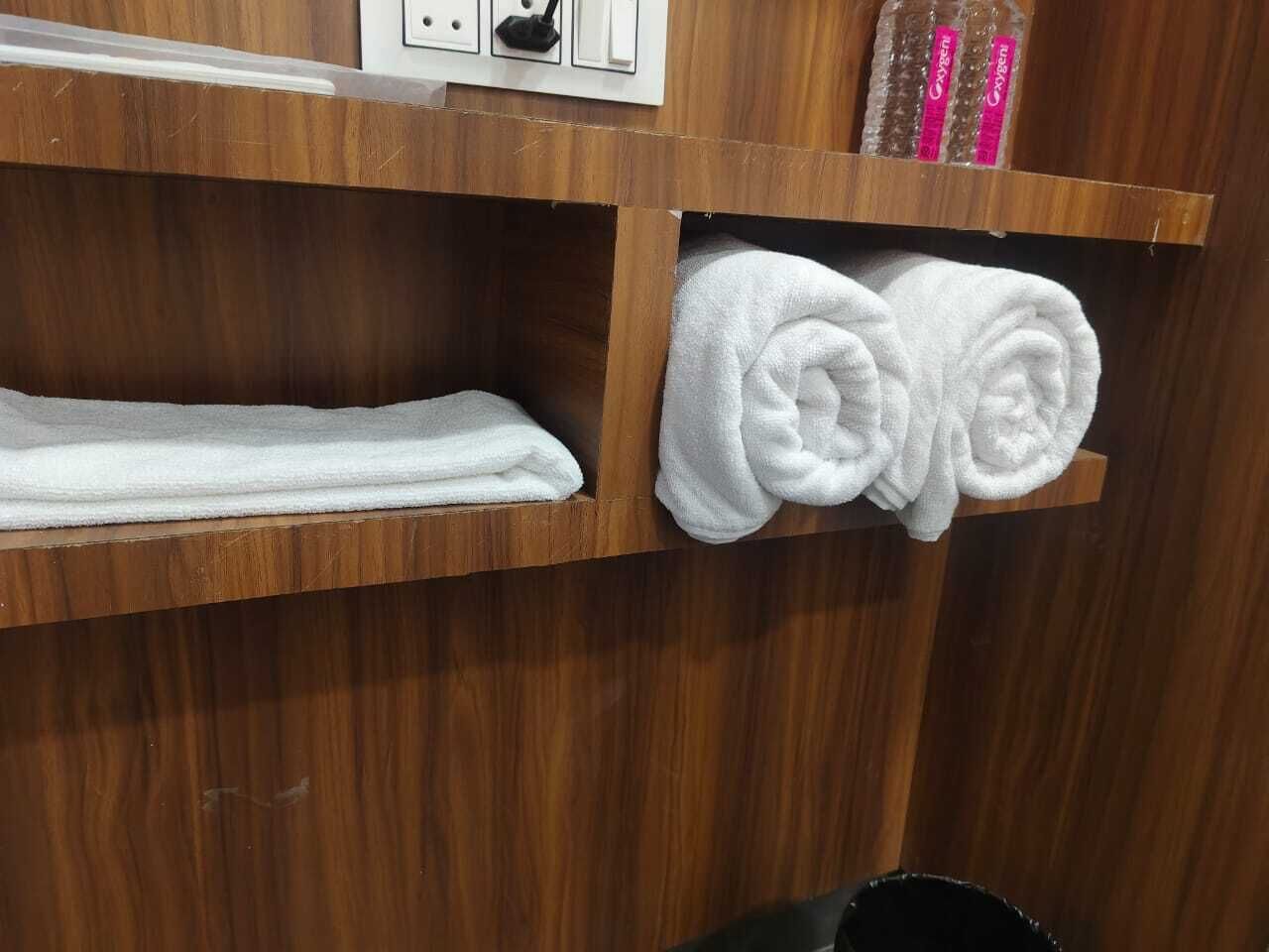 A wooden shelf with a folded white towel and two rolled white towels.