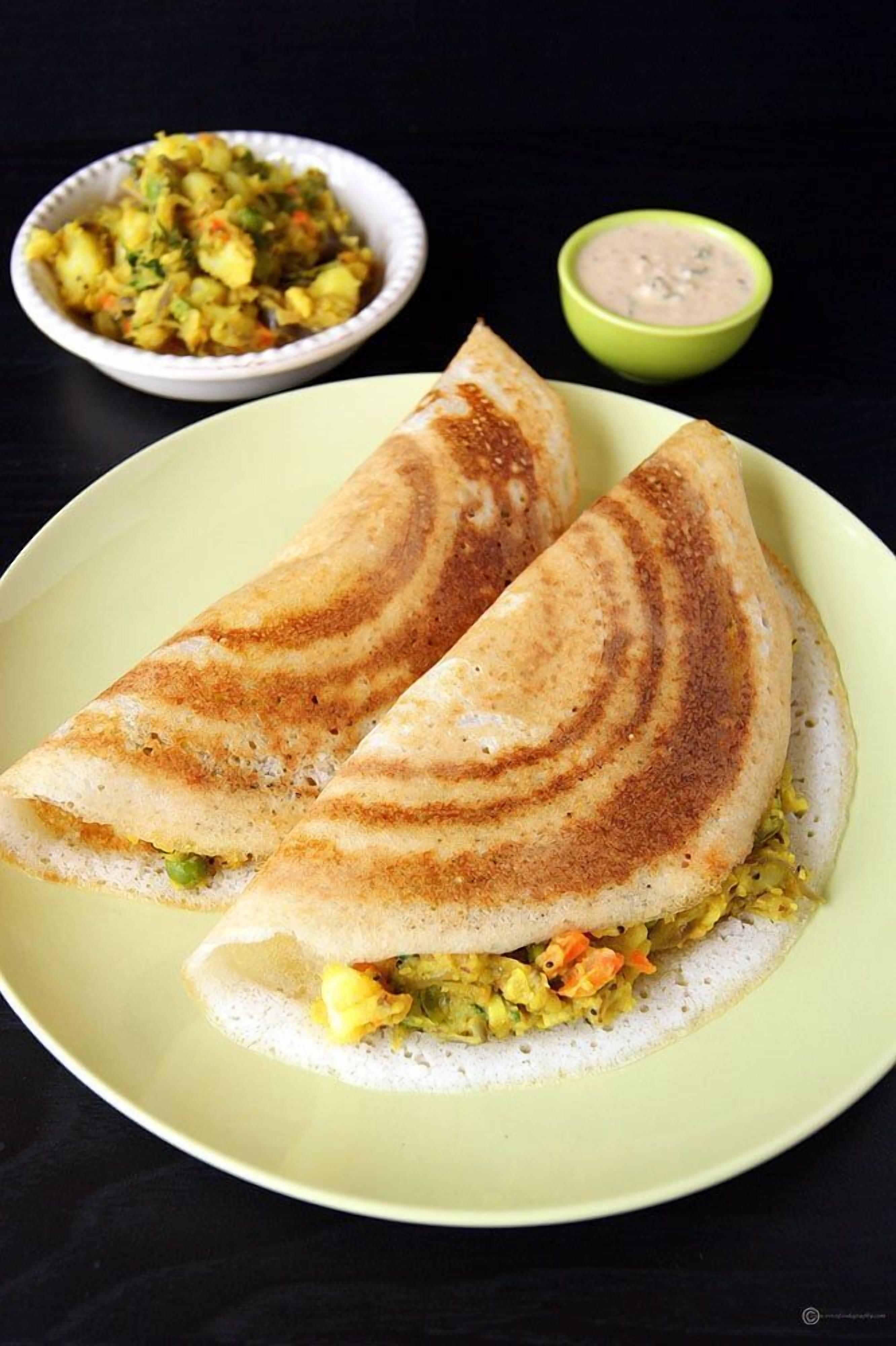 A plate with two folded crepes, a bowl of vegetable curry, and a small bowl of chutney.