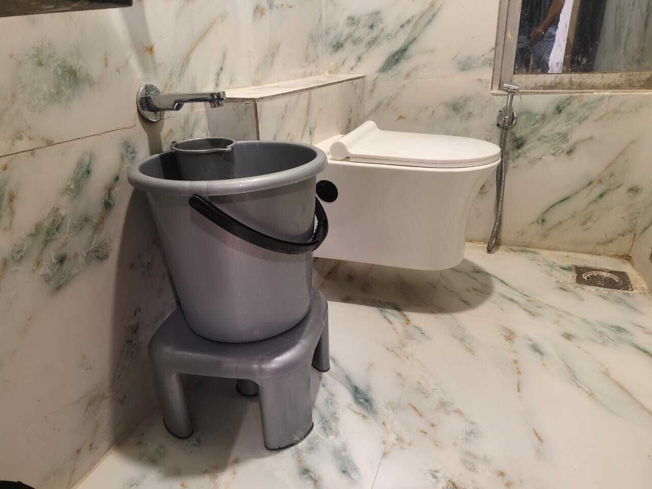 A bathroom with a marble floor, a white toilet, and a grey bucket with a handle.