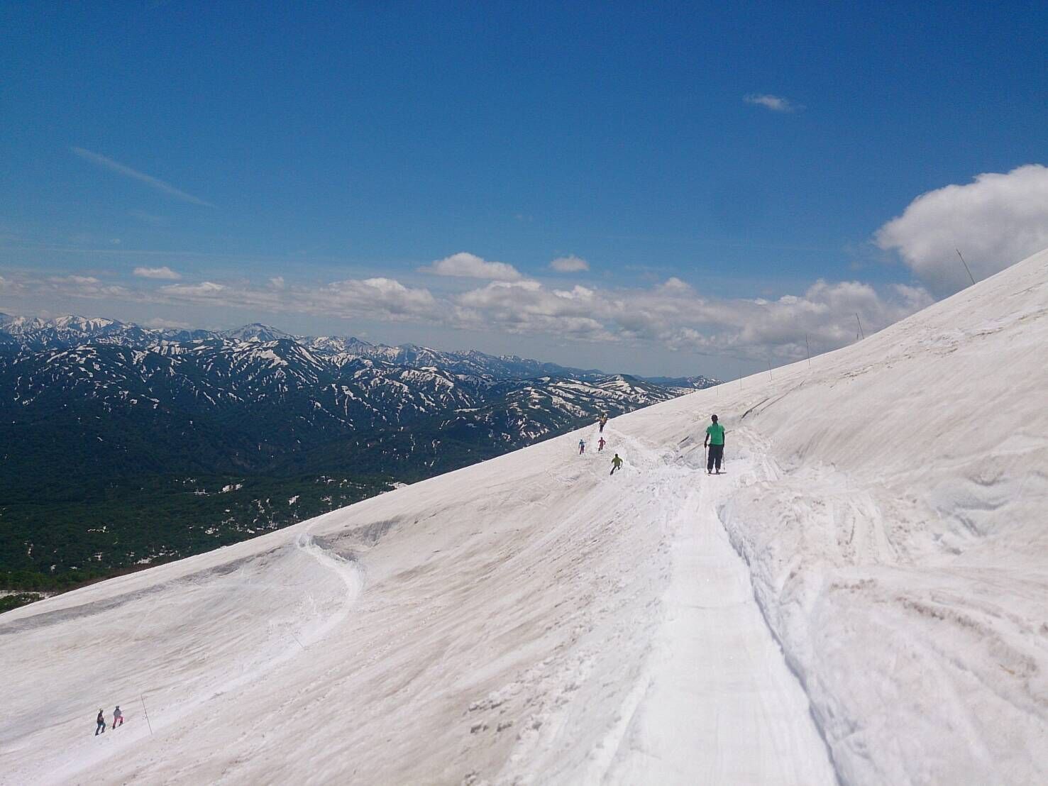 A snow-covered slope with skiers and a clear view of distant mountains.