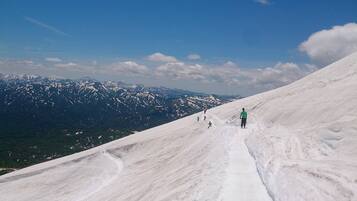 A snow-covered slope with skiers and a clear view of distant mountains.