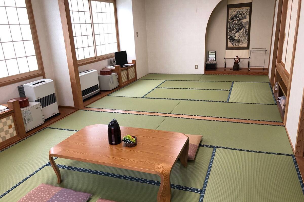 A traditional Japanese room with tatami flooring, a wooden table with a thermos, and a futon bed.