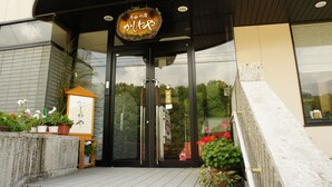 A building entrance with a sign in Japanese, a wooden signboard, and potted plants. - Gassan no yado kasiwaya (Nishikawa)