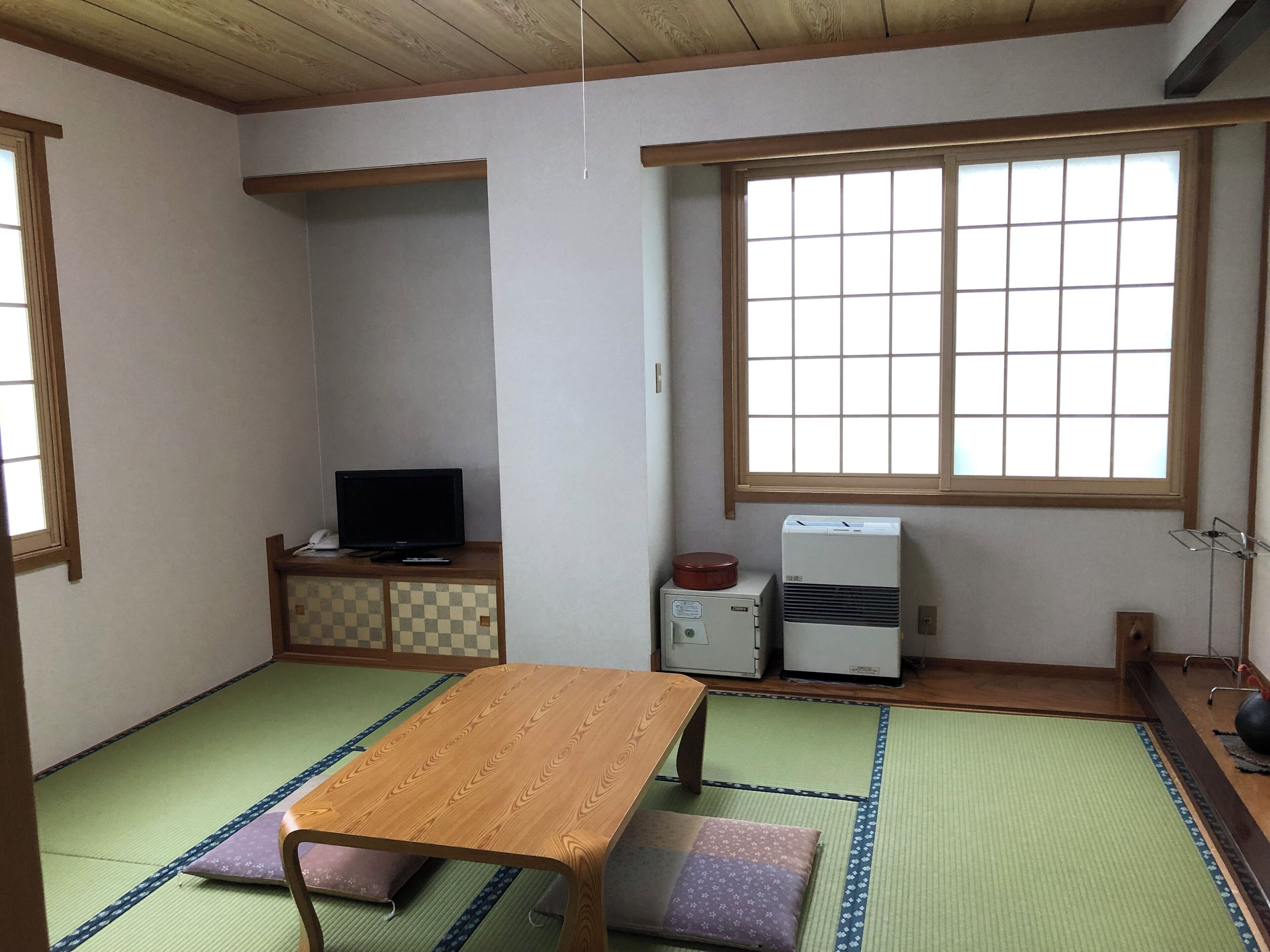 A traditional Japanese room with tatami flooring, a low wooden table, a television, and a small air conditioning unit.