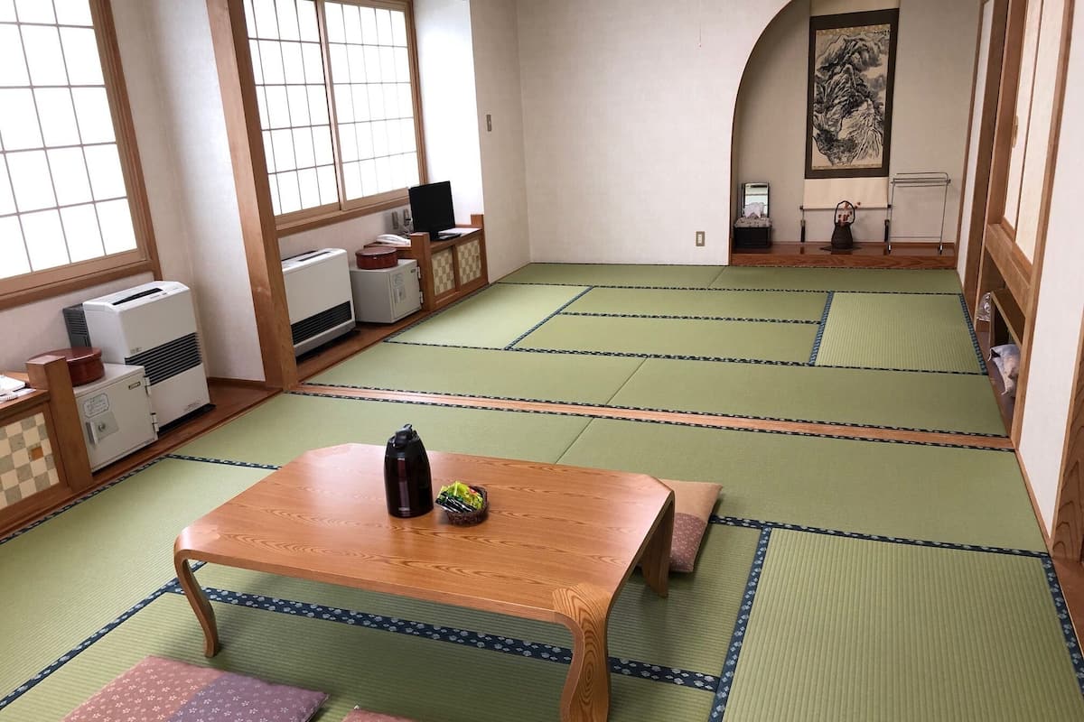 A traditional Japanese room with tatami flooring, a wooden table with a thermos, and a futon bed.