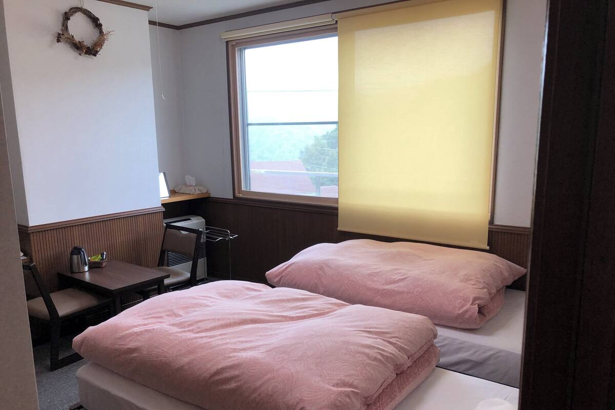 A small, cozy room with two beds, a desk, and a chair.