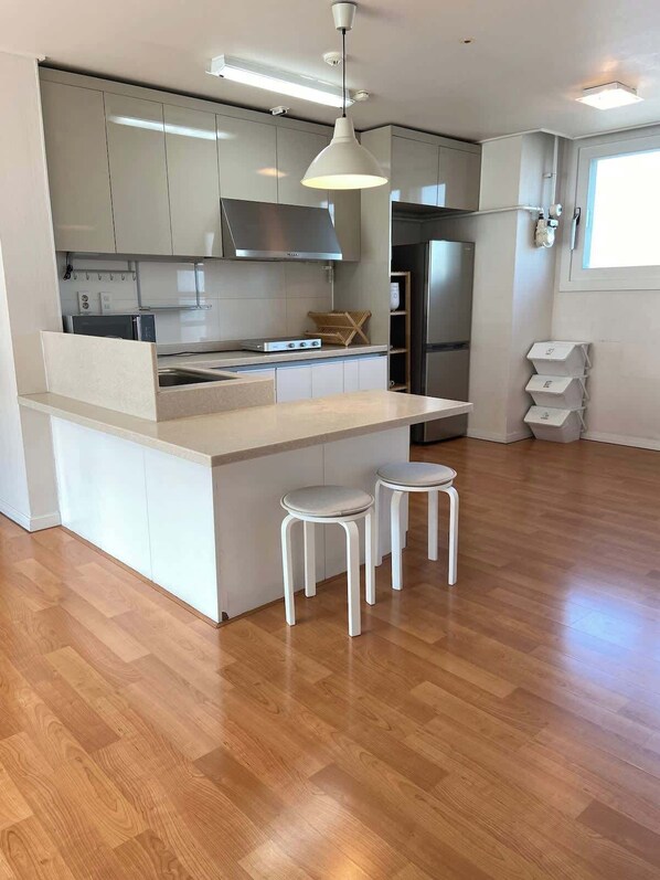 A modern kitchen with white cabinetry, a central island with stools, a stainless steel refrigerator, and a pendant light.