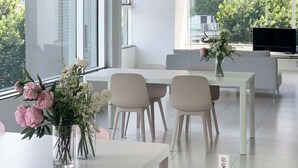 A modern office space with large windows, a white table with chairs, and a vase of flowers.