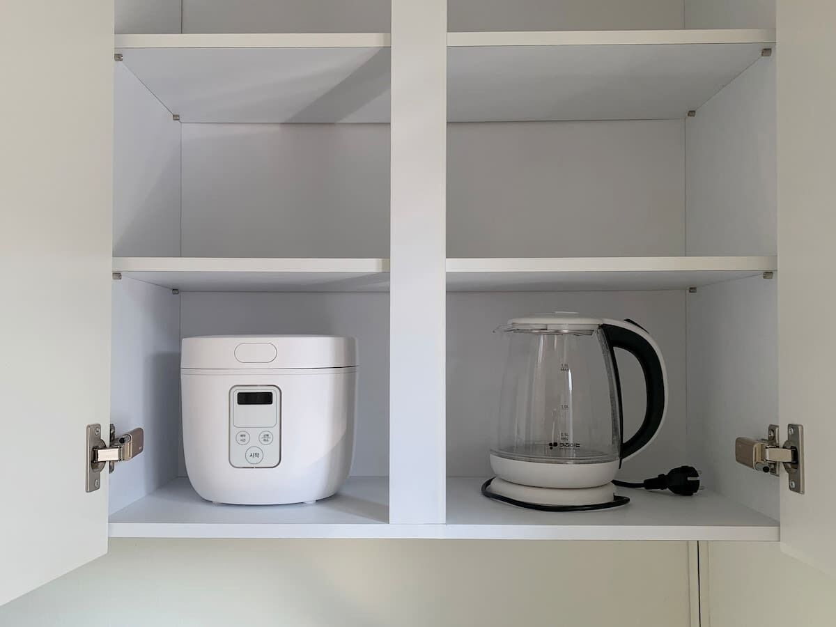 A kitchen with a rice cooker and a blender on open shelves.