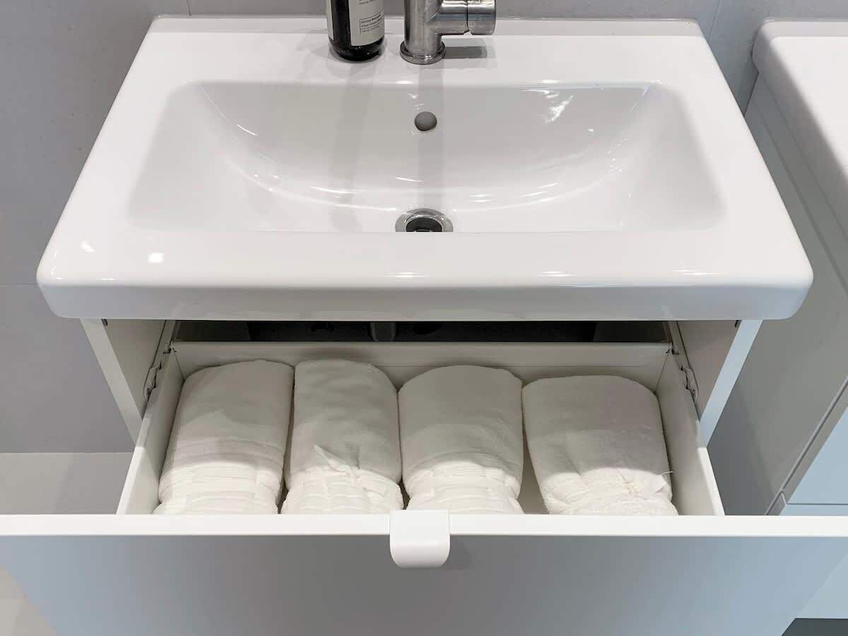 Un lavabo blanc pour la salle de bain, avec un robinet et un tiroir en dessous contenant des serviettes pliées.