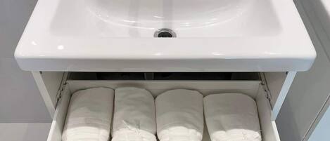 Un lavabo blanc pour la salle de bain, avec un robinet et un tiroir en dessous contenant des serviettes pliées.