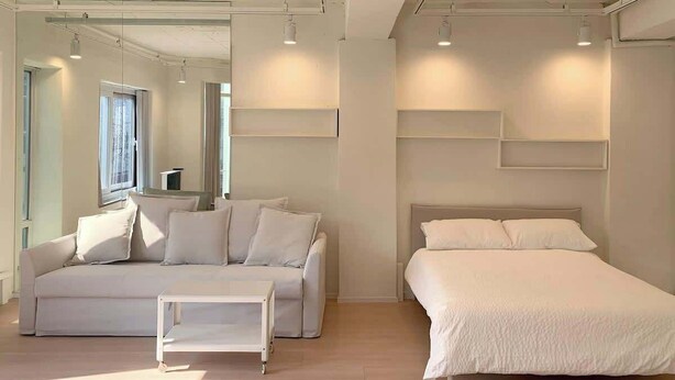 Une chambre moderne avec un canapé blanc, une petite table blanche et un lit avec une literie blanche.