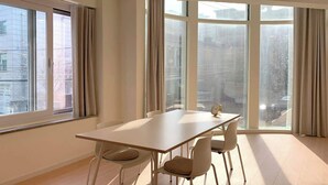 Une pièce avec une grande fenêtre, une table et quatre chaises.