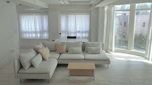 Un salon moderne avec un canapé d’angle, une table basse et de grandes fenêtres dotées de rideaux.