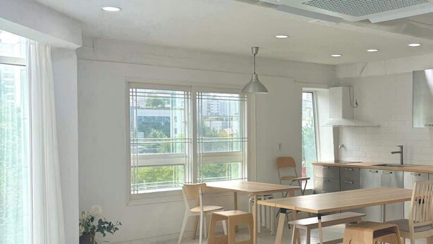 Un salon moderne comprenant un canapé, une table à manger et des chaises, un coin cuisine et de grandes fenêtres offrant une vue dégagée.