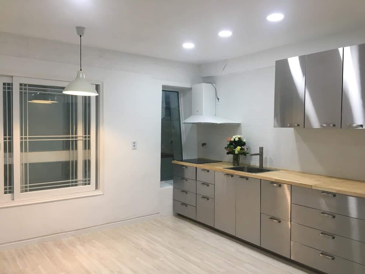 A modern kitchen with a window, stainless steel cabinets, a wooden countertop, and a pendant light.