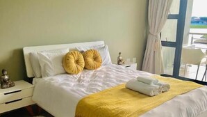 Ein Schlafzimmer mit einem großen Bett, weißer Bettwäsche, einer gelben Decke und einem flauschigen Teppich.