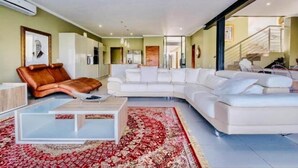 Ein modernes Wohnzimmer mit einem weißen Ecksofa, einem braunen Ledersessel und einem Glastisch.