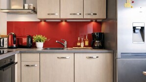 A modern kitchen with stainless steel appliances, wooden cabinets, and a red backsplash. - Charming house - near train station - 6 people (Les Sables-d´Olonne)