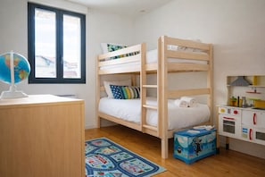 A bunk bed room with a desk, a globe, a window, a toy kitchen set, and a school-themed rug.